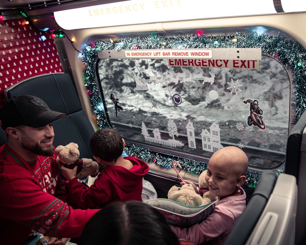 A volunteer handing teddy bears to children by a decorated train window