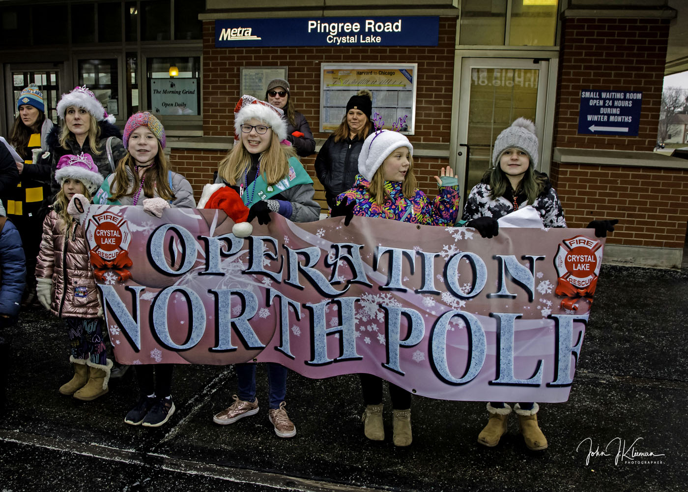 Girls holding the Operation North Pole banner at Pingree Road station