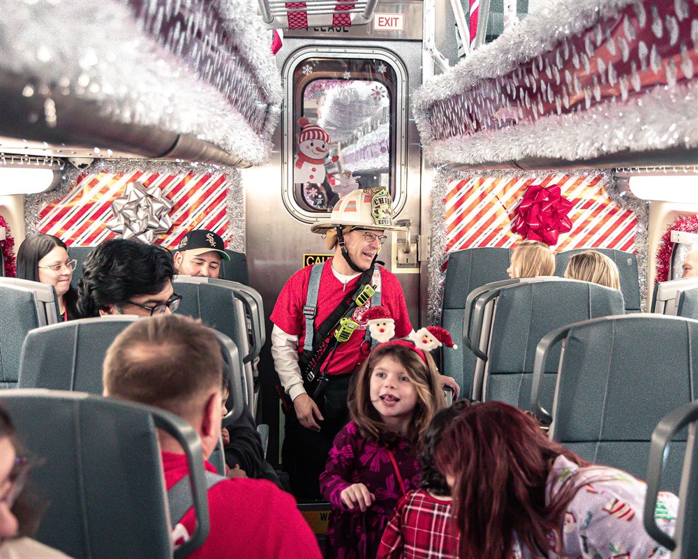 A firefighter chief greeting families inside a Christmas-decorated train car