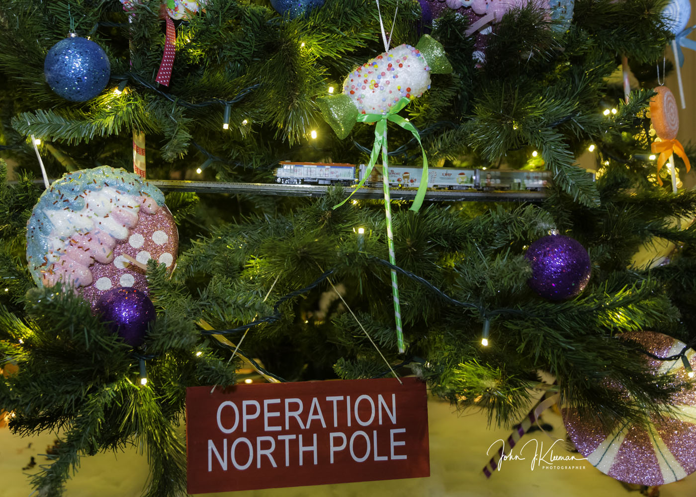 Close-up of an Operation North Pole decorated Christmas tree with candy ornaments, twinkle lights, and a model train running through the branches