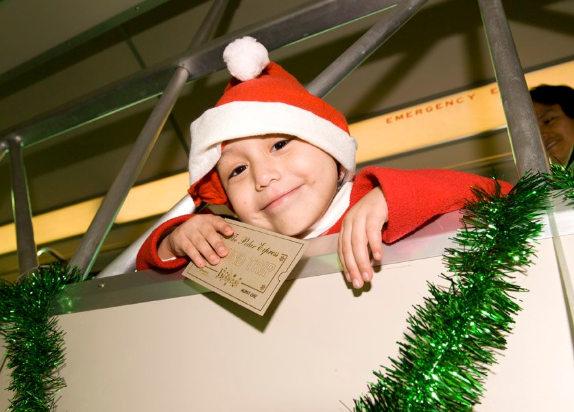 Child in a Santa hat smiling and holding a Polar Express ticket aboard the holiday train