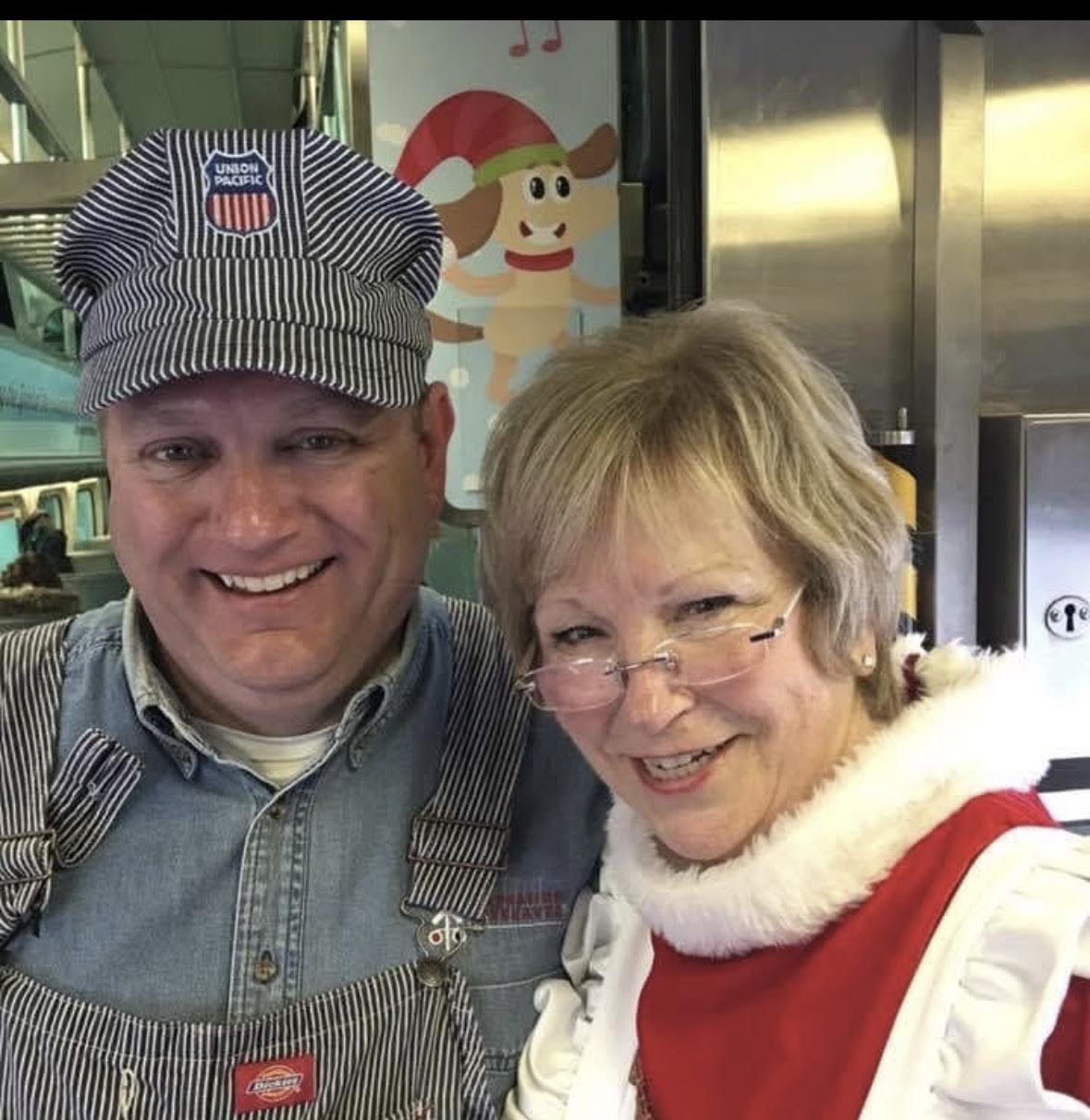 A conductor volunteer and Mrs. Claus smiling together aboard the North Pole train