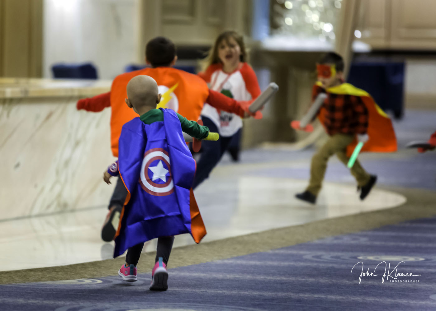 Children in superhero capes running through the event hall