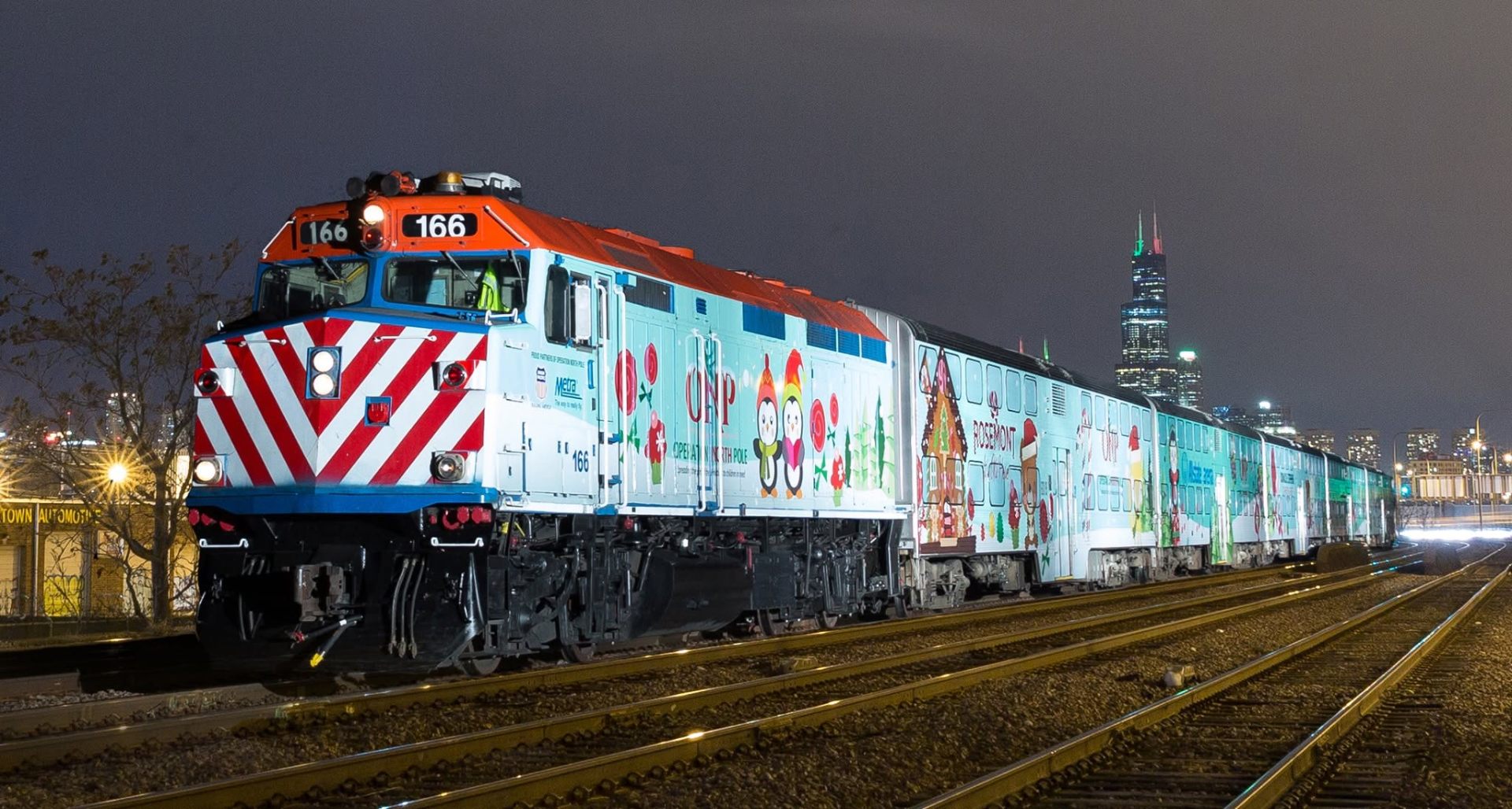 The Operation North Pole Metra train lit up at night with the Chicago skyline