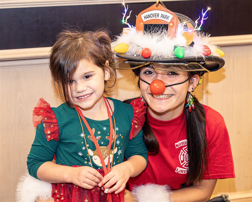 A smiling child with a volunteer in a Hanover Park firefighter reindeer hat at Operation North Pole