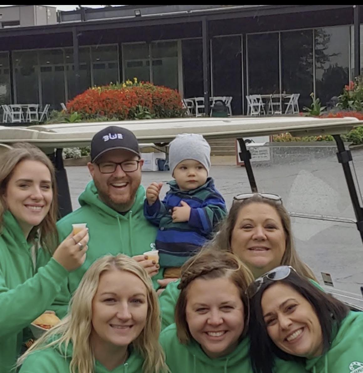 Operation North Pole volunteers in green sweatshirts smiling with a young child