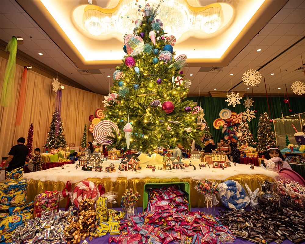 A towering Christmas tree decorated with candy ornaments above a miniature holiday village and tables piled with candy at Operation North Pole