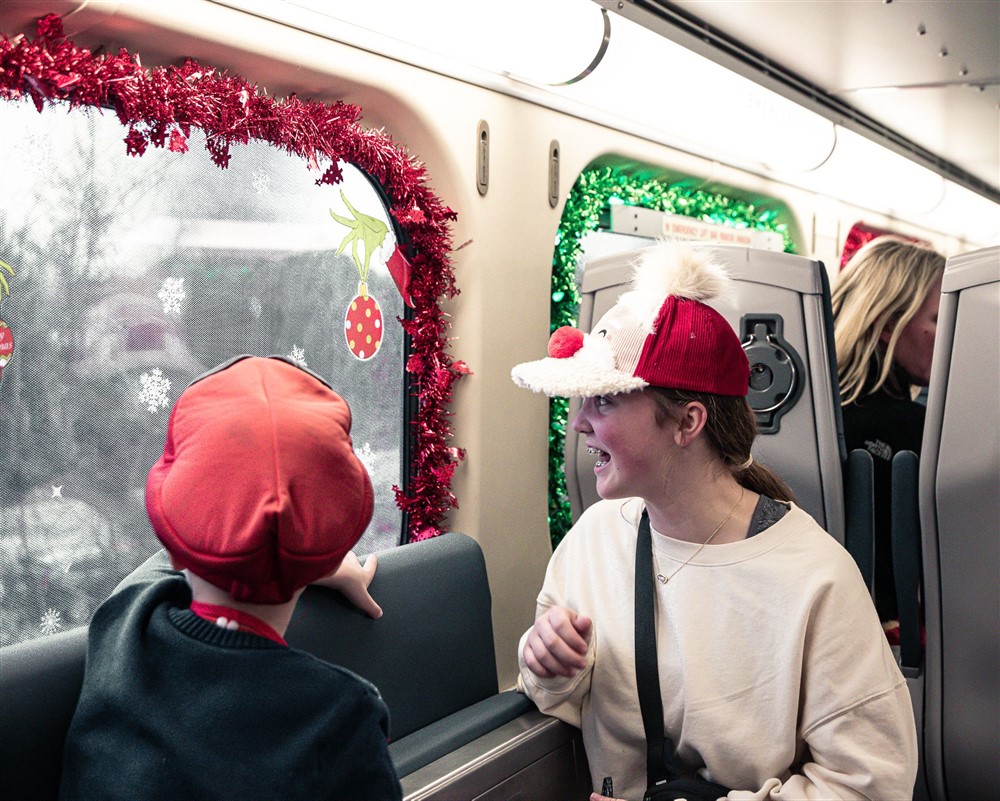 A volunteer in a reindeer hat laughing with a child on the decorated train
